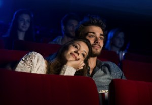 Young loving couple at the cinema watching a movie, he is hugging her girlfriend