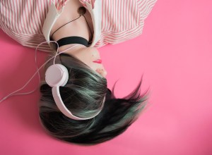 mujer con cabello en la cara audifonos rosas y fondo rosa 